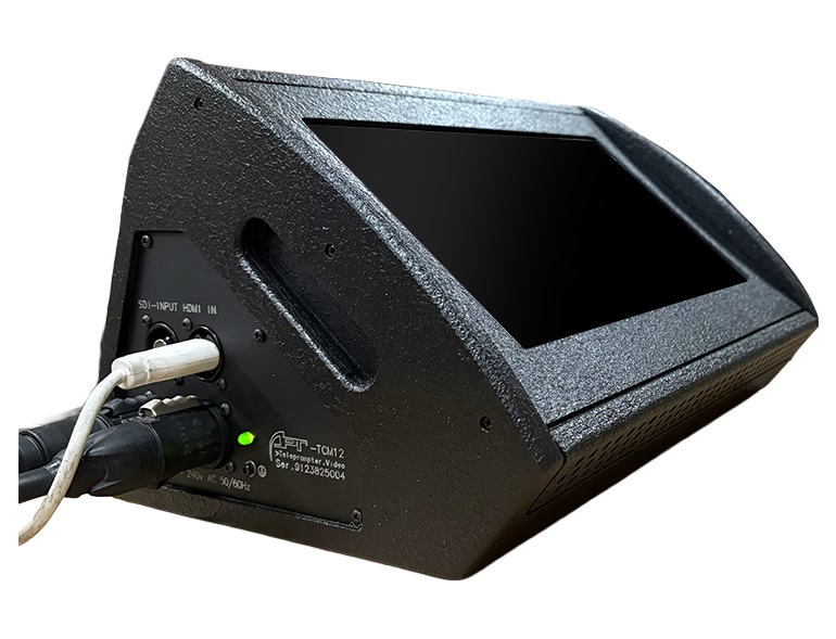 Black angled video monitor on a wooden surface with HDMI/SDI cables plugged in and a green power light visible on the back panel.
